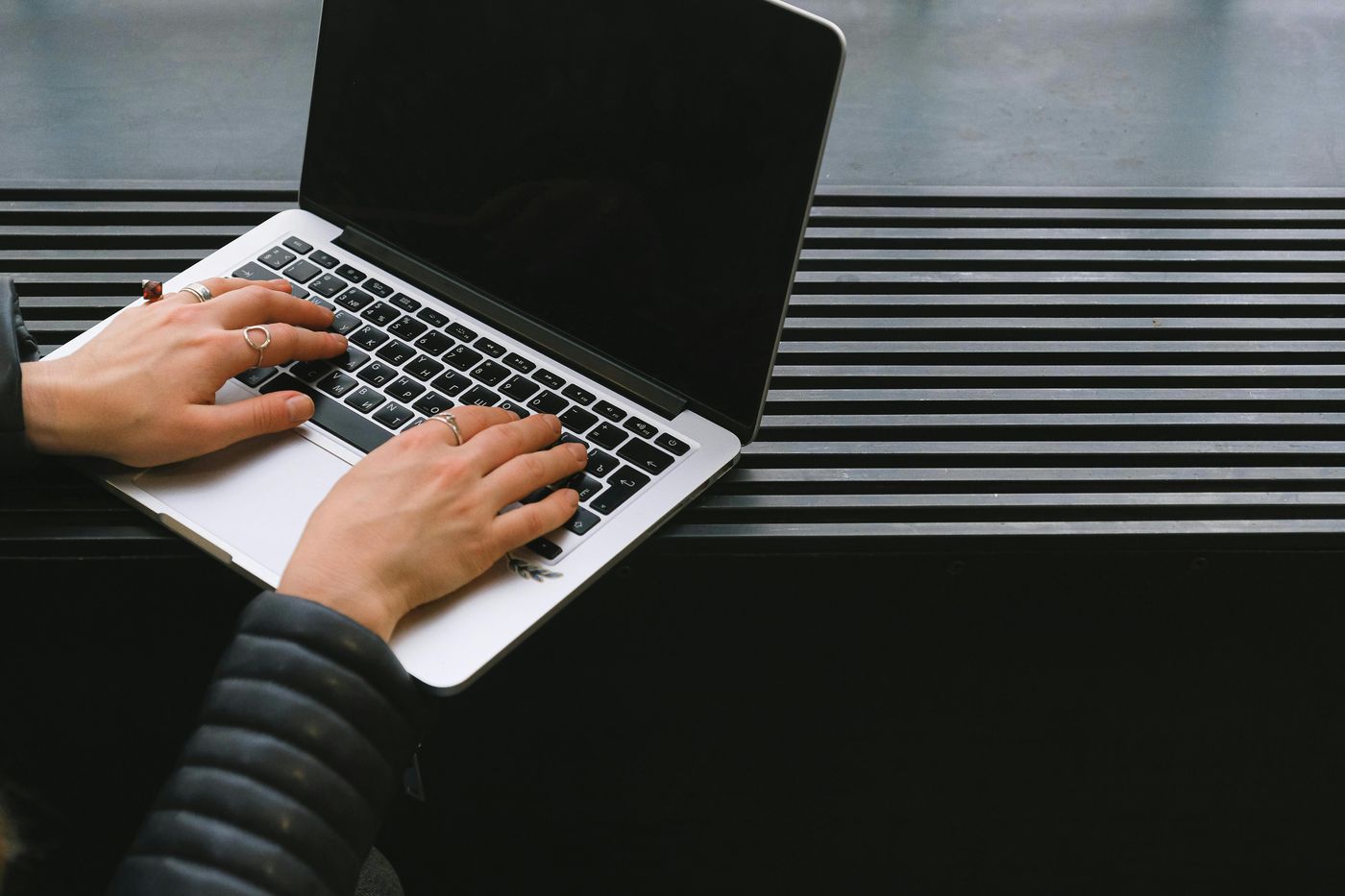 A woman’s hands typing on a laptop keyboard with a darkened screen